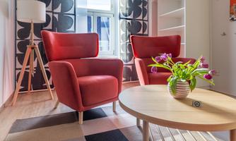 A modern living room with two red armchairs and a round coffee table. On the table, there is a vase with fresh tulips.