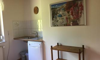 A bright kitchen with a sink and a dishwasher. On the wall hangs a picture of a picturesque Greek landscape.