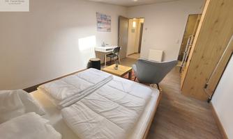 A bright room with two separate beds and a modern armchair. The room has a table and has access to the bathroom.