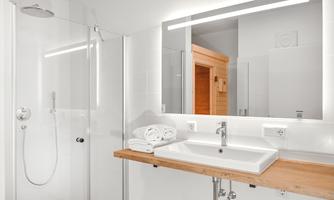A modern bathroom with a shower and a large mirror. The wash area is made of wood and there are fresh towels available.