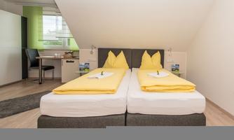 A modern room with two single beds and yellow bedcovers. The room is bright and minimally furnished.