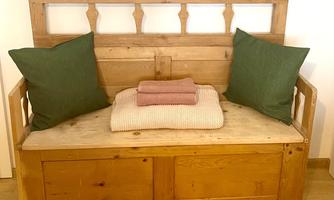 A cozy wooden bench with green cushions. On it lie a blanket and two towels.