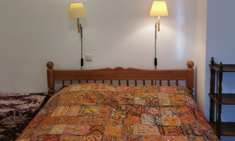A cozy bedroom with a wooden bed and a colorful, patterned bedspread. Lamps are hanging on the walls, creating a warm atmosphere.