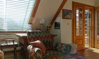 A bright, cozy living room with large windows and a wood ceiling. A colorful armchair and a table create an inviting atmosphere.