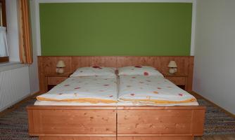 A cozy bedroom with a large wooden bed and colorful bedding. On the walls are two bedside lamps and a green accent wall.