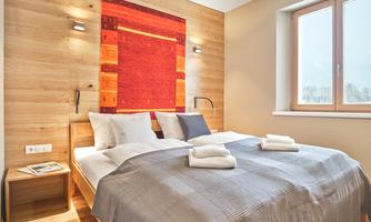 A modern bedroom with a double bed and wood-paneled walls. The room design is bright and cozy, with a large window.