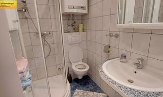 A modern bathroom with a shower, a sink, and a toilet. The walls are tiled with white tiles and there is a large mirror.