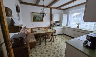 A cozy kitchen with a dining table and chairs. The room has a wooden ceiling and large windows that let in a lot of light.