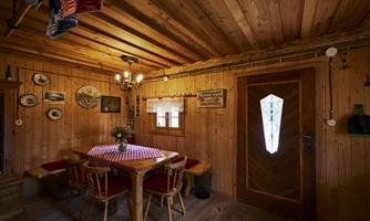 A cozy wooden cabin with a round table and chairs. Pictures hang on the walls, and a window lets in light.