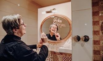 A person stands in front of a mirror in the bathroom and smiles. "Good morning" is written on the mirror.