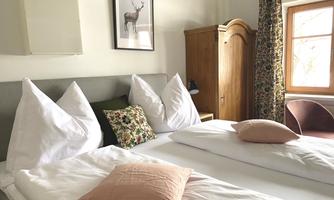 A cozy bedroom with two beds and elegant pillows. The room is bright and includes a wardrobe as well as decorative curtains.