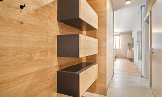 A modern hallway with wood panels and minimalist shelves. The walls are light, and there is a clear view of the adjoining room.
