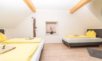 Cozy bedroom with two single beds and soft yellow cushions. A window with a small orchid creates an inviting atmosphere.
