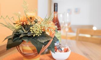 A beautiful bouquet in a striped pot is on a table. In the background, there is a bottle of wine and two glasses visible.