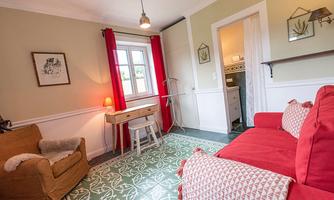 A cozy room with a red sofa and a small table. Large windows let in plenty of light and it is tastefully decorated.