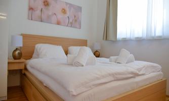A cozy bedroom with a large bed and light wood. The walls are decorated with a gentle image of flowers, and light streams in through the window.