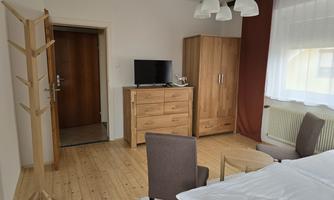 A cozy room with a wooden table, two chairs, and a wardrobe. There is a television and a coat rack on the wall.