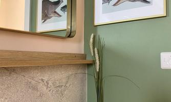 A modernly designed room with a green wall and a wooden shelf. Two pictures of a fish hang on the wall, and a vase with dried flowers stands on the shelf.
