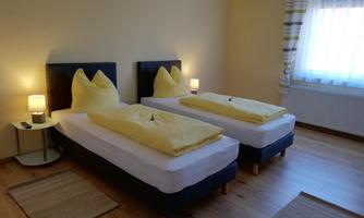 A cozy bedroom with two single beds and yellow bedspreads. Large windows provide plenty of daylight.