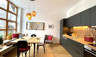 A modern kitchen with wooden surfaces and dark cabinets. The dining area is bright and cozy with large windows.