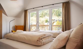 A cozy bedroom with a large window and a view of the surrounding mountains. The bed is neatly made with blankets and pillows.