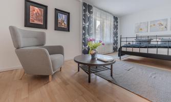 A modern bedroom with a bed and an elegant armchair. A round table with fresh flowers and artworks on the wall complete the space.