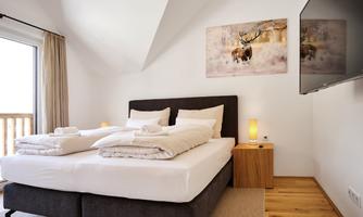 A modern bedroom with a double bed and a flat-screen TV. Large windows let in plenty of light and create an inviting atmosphere.