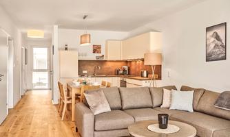 A modern apartment with a cozy seating area and an open kitchen. Bright colors and hardwood floors create an inviting atmosphere.