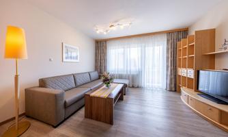 A modern living room with a beige sofa and a wooden coffee table. Large windows provide plenty of daylight and a cozy atmosphere.