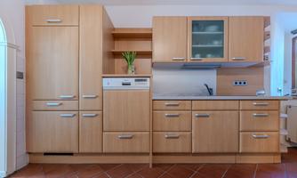 Modern kitchen made of light wood with refrigerator, dishwasher, and built-in stove. The kitchen is functional and well-organized.