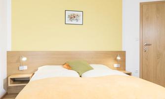A modern bedroom with a wooden bed and a yellow wall. There are bedside lamps and a small wall decoration.