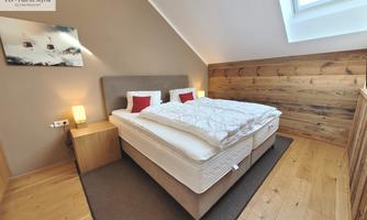 A cozy bedroom with a large bed and modern furniture. The walls are bright, and the wood creates a warm atmosphere.