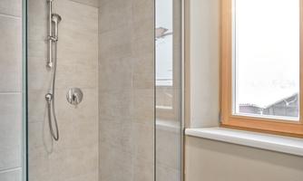 A modern shower in a bright bathroom. The walls are designed in neutral tones and light falls through a window.