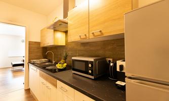 A modern kitchen with wooden cabinets and a dark workspace. There is a refrigerator, a microwave, and a sink.