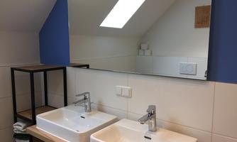 A modern bathroom with two sinks and a large mirror. The walls are kept in plain colors, and towels are neatly stacked.
