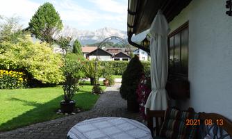 A quiet garden with green lawns and colorful flowers. In the background, mountains and a cozy seating area can be seen.