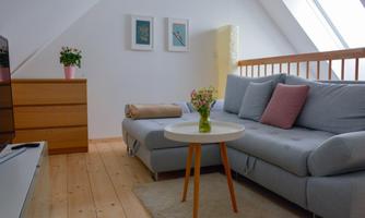 A cozy living room with a gray sofa and a round table. Pictures are hanging on the wall, and there is a wooden floor as well as a wardrobe.