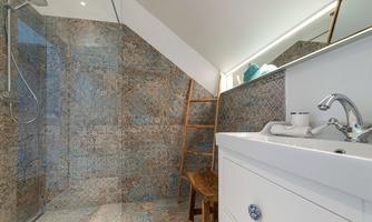 A modern bathroom with a walk-in shower and elegant tiles. A wooden chair and accessories on the windowsill complement the harmonious design.