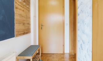 A bright corridor with wooden flooring and a modern coat rack. On the left side, there is a bench with storage.