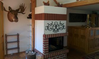 A cozy interior with a fireplace made of red bricks. On the wall hangs a deer antler, and in the background, you can see wooden shelves and a kitchenette.