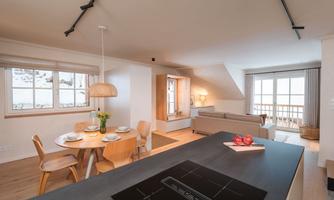 A modern, bright apartment with an open kitchen and dining area. Large windows provide a view of the mountains and ensure plenty of daylight.