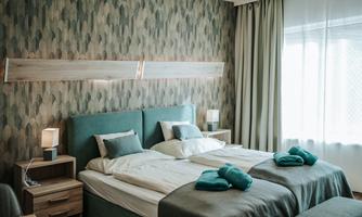 Bright and modern bedroom with two beds. The walls are decorated with a simple pattern and there are green towels on the bed.