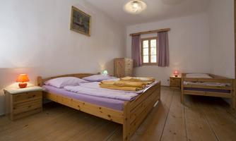 A cozy bedroom with two wooden beds and natural light. The walls are light, and there is simple decoration with a picture and curtains.