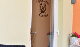 A glass door with a logo for "Schmieder Zimmer". The entrance area is brightly and friendly designed.