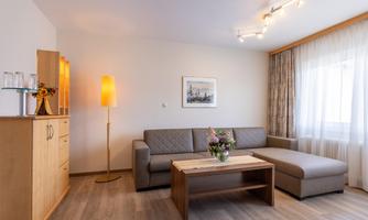 A modern living room with a gray sofa and a wooden table. Large windows let in a lot of light, and the decor is minimalist and inviting.