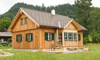 A cozy wooden house with green shutters in a picturesque setting. Surrounded by meadows and trees, it radiates rural charm.