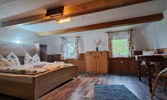 A cozy bedroom with a double bed and wooden decor. There are windows with curtains and a small table in the room.