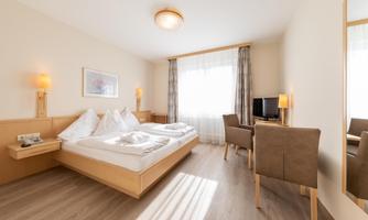 A bright, modern bedroom with a double bed and two cozy chairs. Large windows let in plenty of natural light.