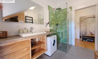 A modern bathroom with a shower and a washing machine. The walls are partially fitted with green tiles, and there is a large mirror.