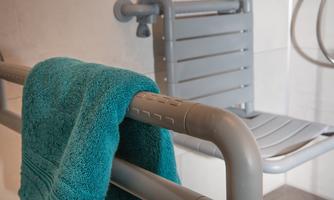 A shower area with a gray shower seat and a turquoise towel. The seat is mounted on the wall and provides safety while showering.